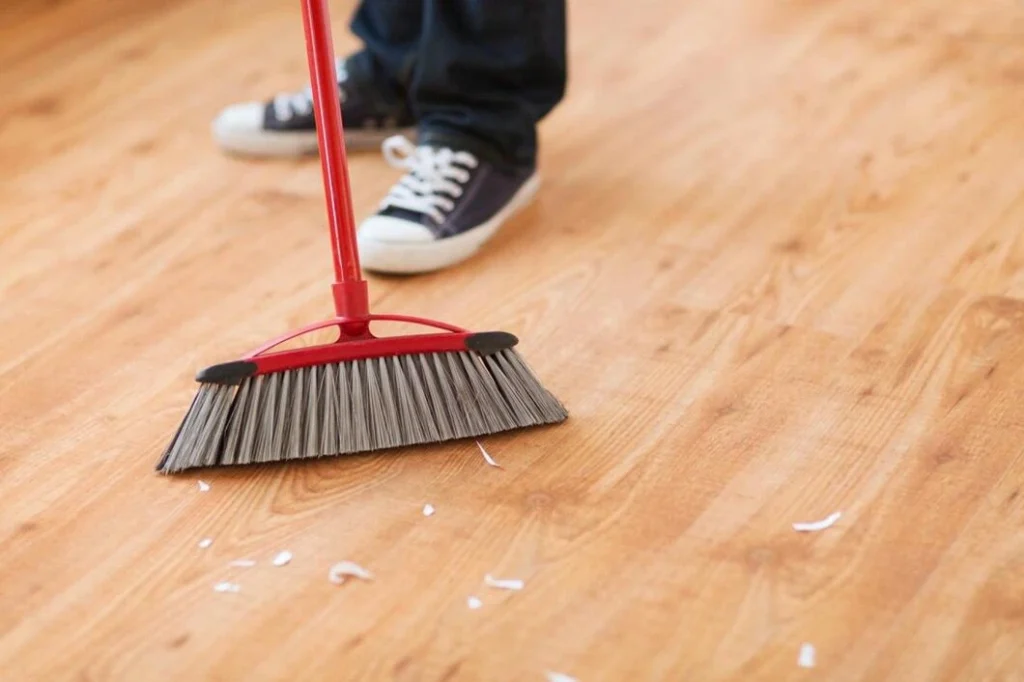 Person unsafely cleaning wood flooring with a hard hand broom